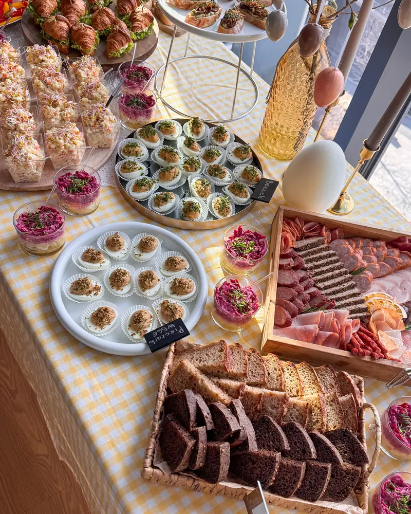 Wędliny w drewnianej skrzynce, pieczywo i faszerowane jajka na stole w żółtą kratkę